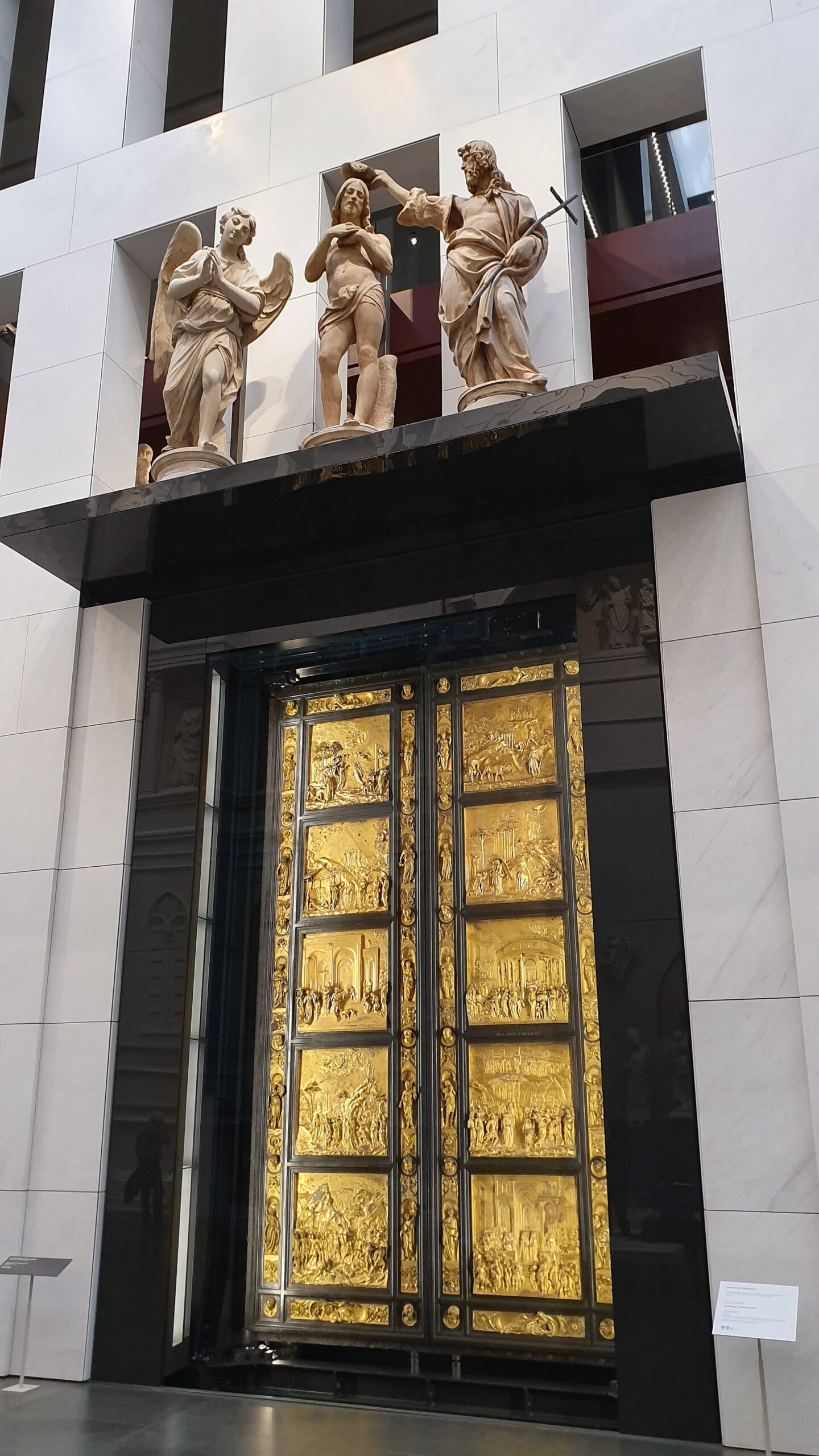 Ghiberti's gilded Gates of Paradise stand behind glass in Florence's cathedral museum, with ten relief panels and a sculpture group above.