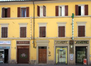 A green cross and black-and-gold pharmacy signs mark the yellow frontage of Florence's Farmacia del Mercato Centrale.
