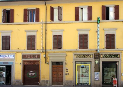 A green cross and black-and-gold pharmacy signs mark the yellow frontage of Florence's Farmacia del Mercato Centrale.
