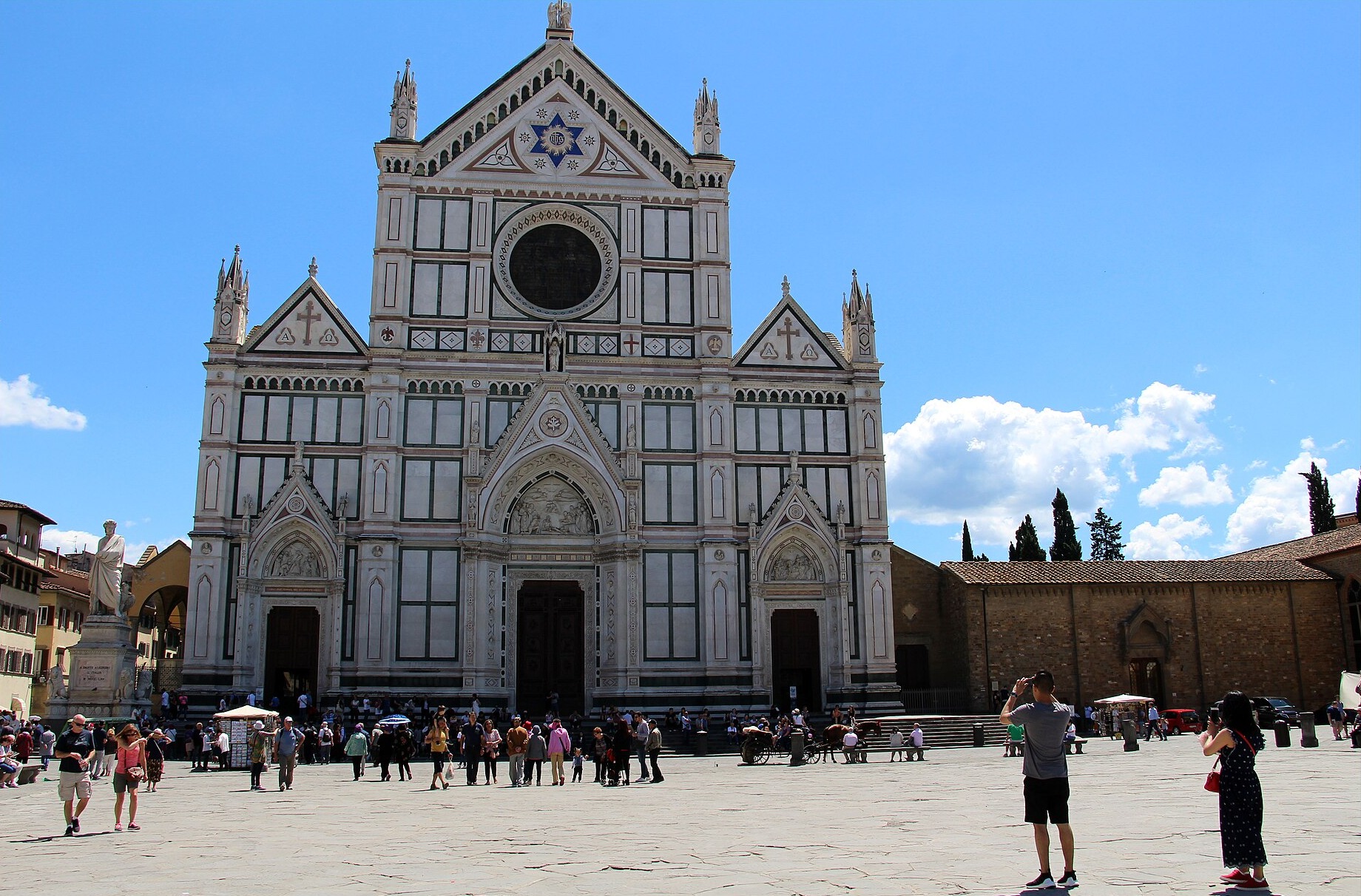 Groups of visitors gather outside Santa Croce’s entrance steps beneath the patterned marble facade in Florence on a sunny day.