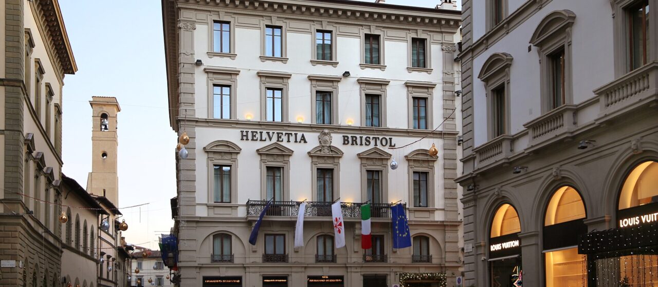 Helvetia and Bristol’s pale palazzo facade rises above a Florence street, with hotel lettering and flags across its balcony.