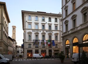 Helvetia and Bristol’s pale palazzo facade rises above a Florence street, with hotel lettering and flags across its balcony.