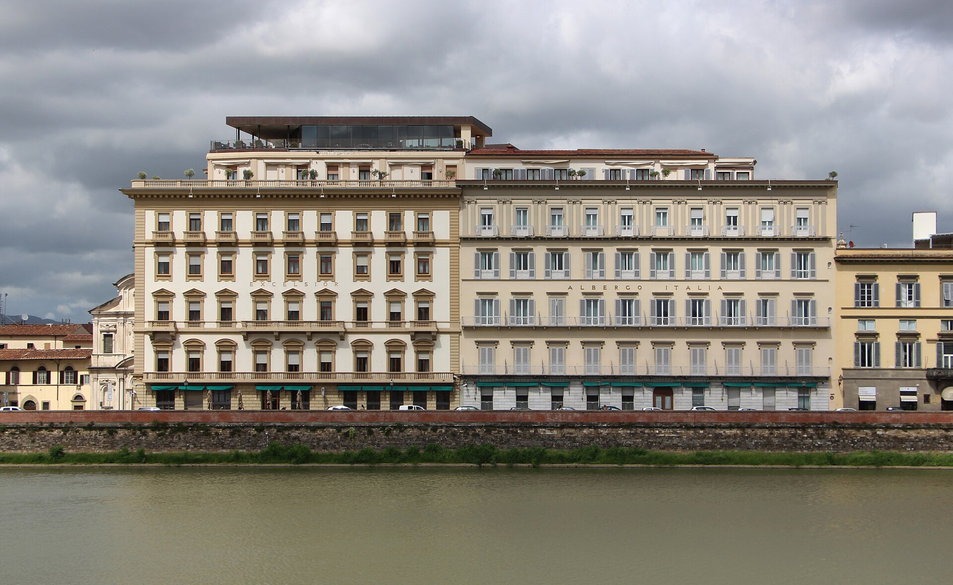 Hotel Excelsior’s pale river-facing facade stands above the Arno embankment in Florence beneath a cloudy sky.