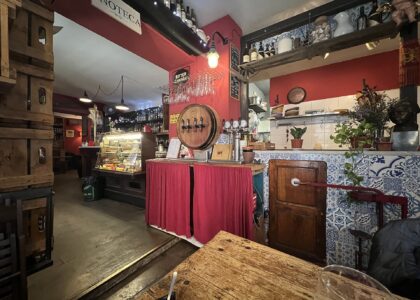 Inside a red-walled Florence wine bar with an enoteca sign, a barrel-fronted tap, bottles on shelves, a glass cabinet and tiled counter.