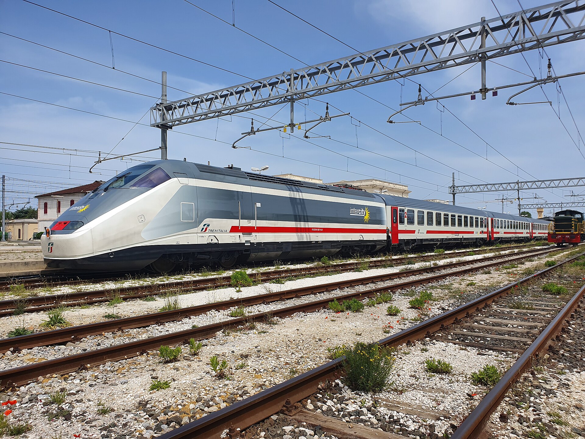 A silver and grey electric locomotive heading a rake of white and red Intercity coaches beside an empty platform at Livorno Centrale