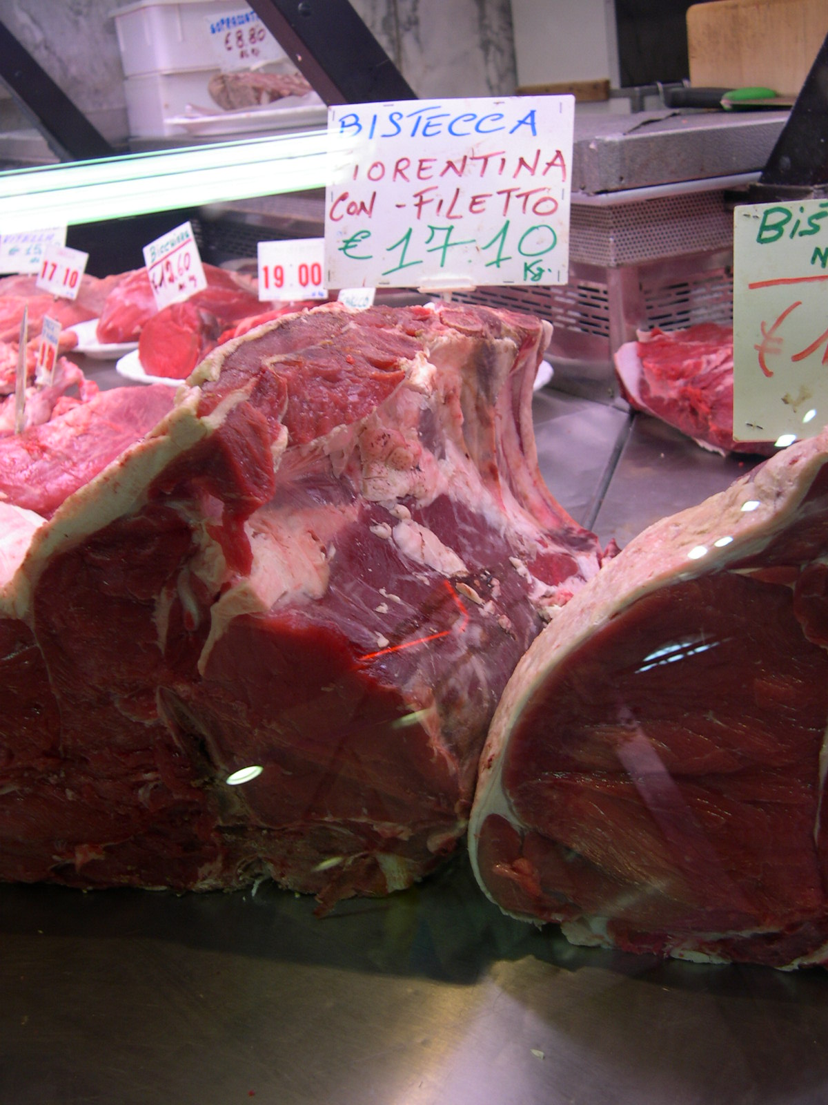 Large raw beef cuts fill a glass butcher's display case beneath handwritten labels at Florence's Mercato Centrale.