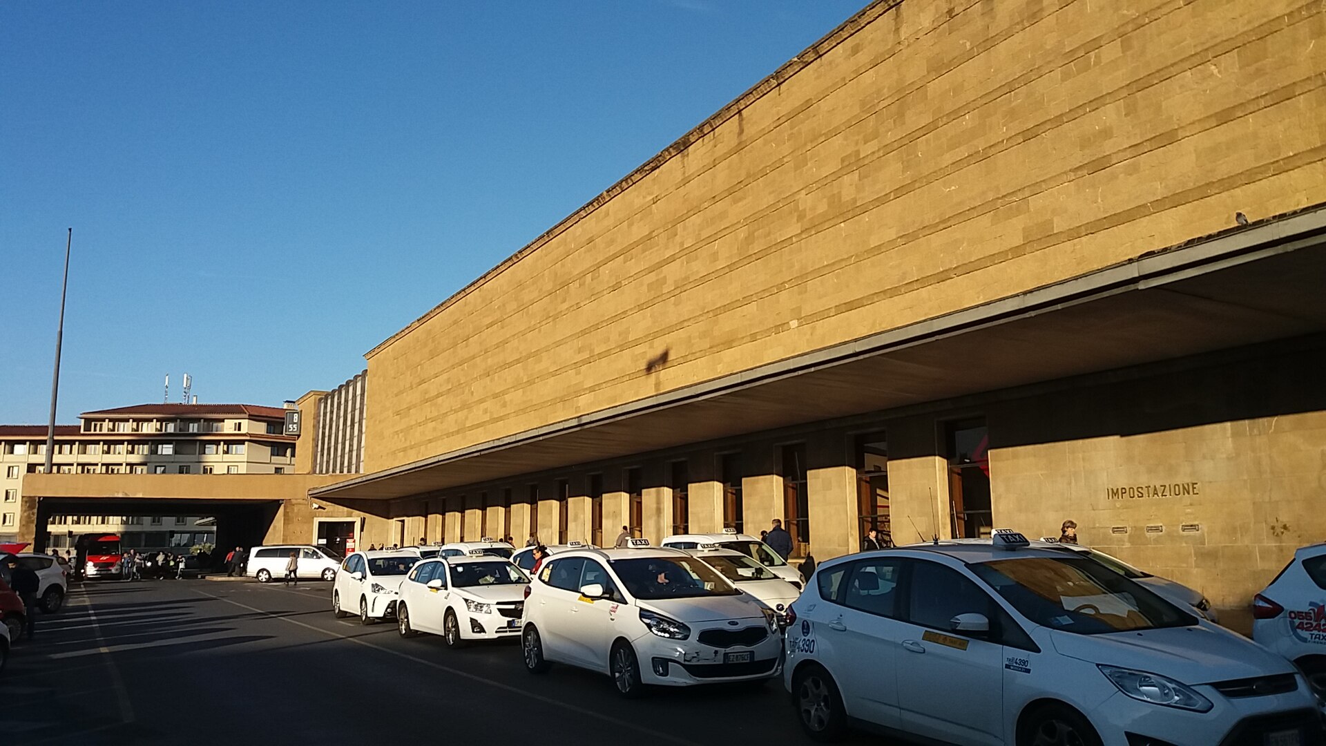A line of white taxis with roof signs waits beneath the stone frontage of Santa Maria Novella station in Florence.