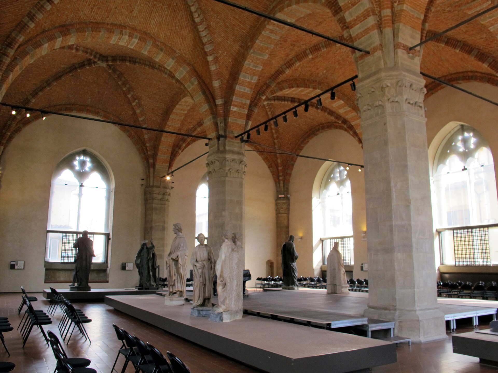 Marble and bronze statues stand beneath brick vaults and pointed windows in Florence's Orsanmichele sculpture museum.