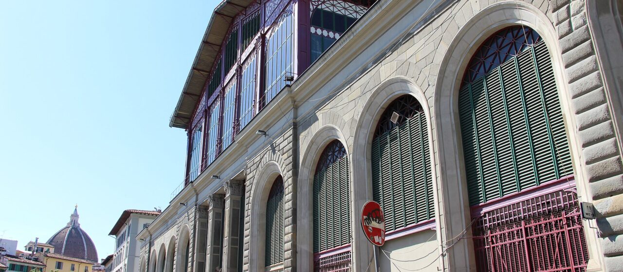 Mercato Centrale's stone arches, green shutters and red iron upper structure line a sunny street in central Florence.