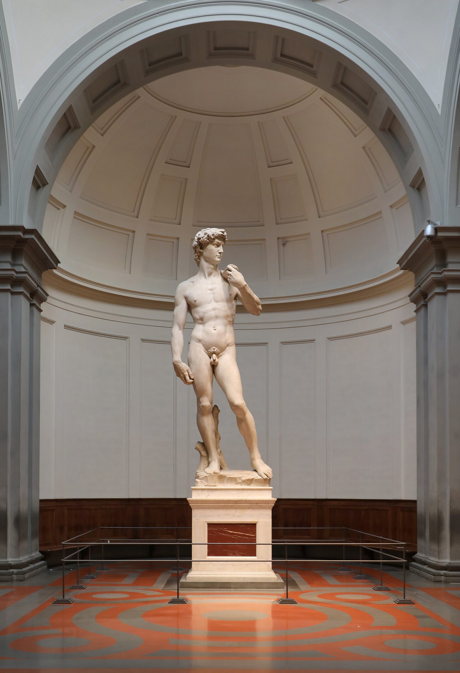 Michelangelo's David stands on a pedestal against the curved white walls of the Accademia Tribune in Florence.