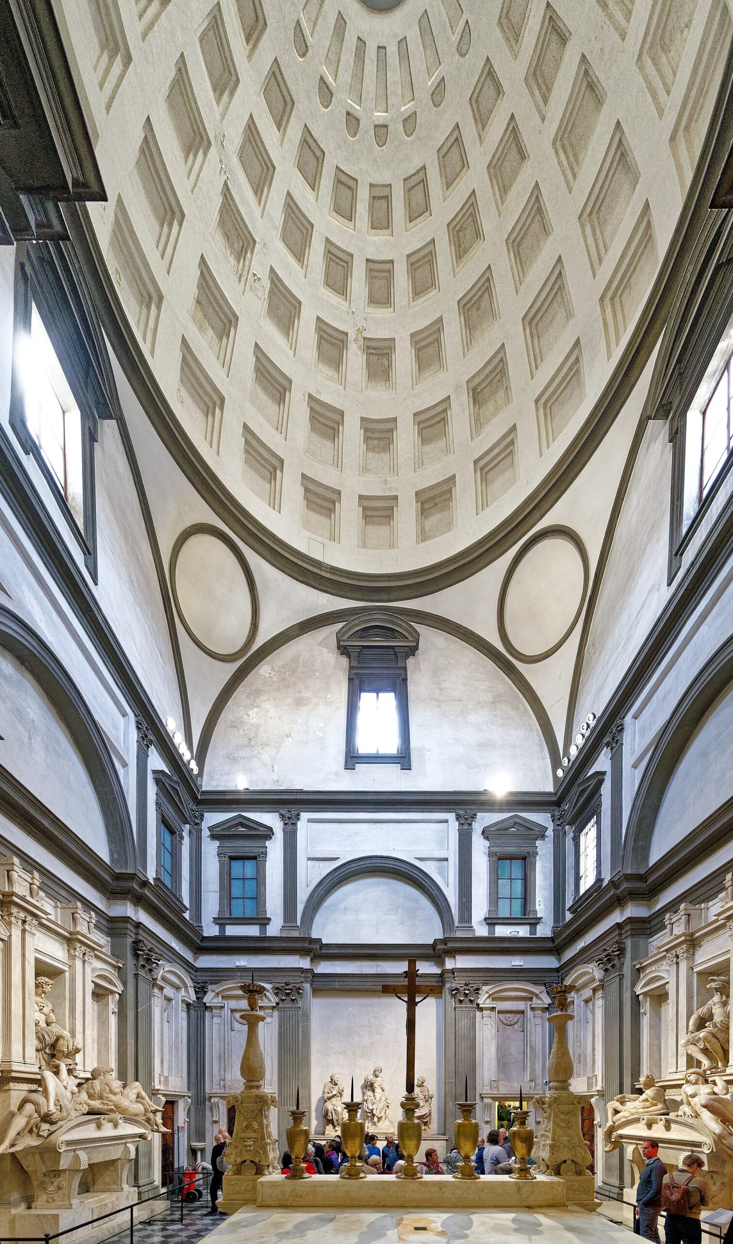 Michelangelo's Medici tombs flank visitors beneath the coffered dome of the New Sacristy at San Lorenzo in Florence.