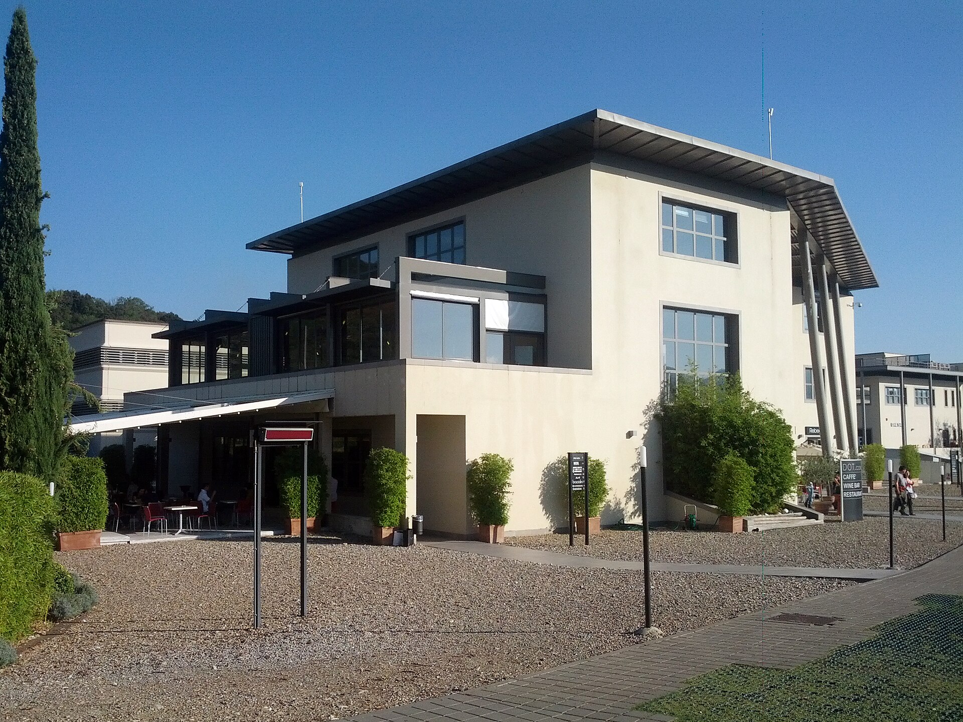 A modern building and shaded terrace border the cobbled pedestrian paths at The Mall outlet in Reggello.
