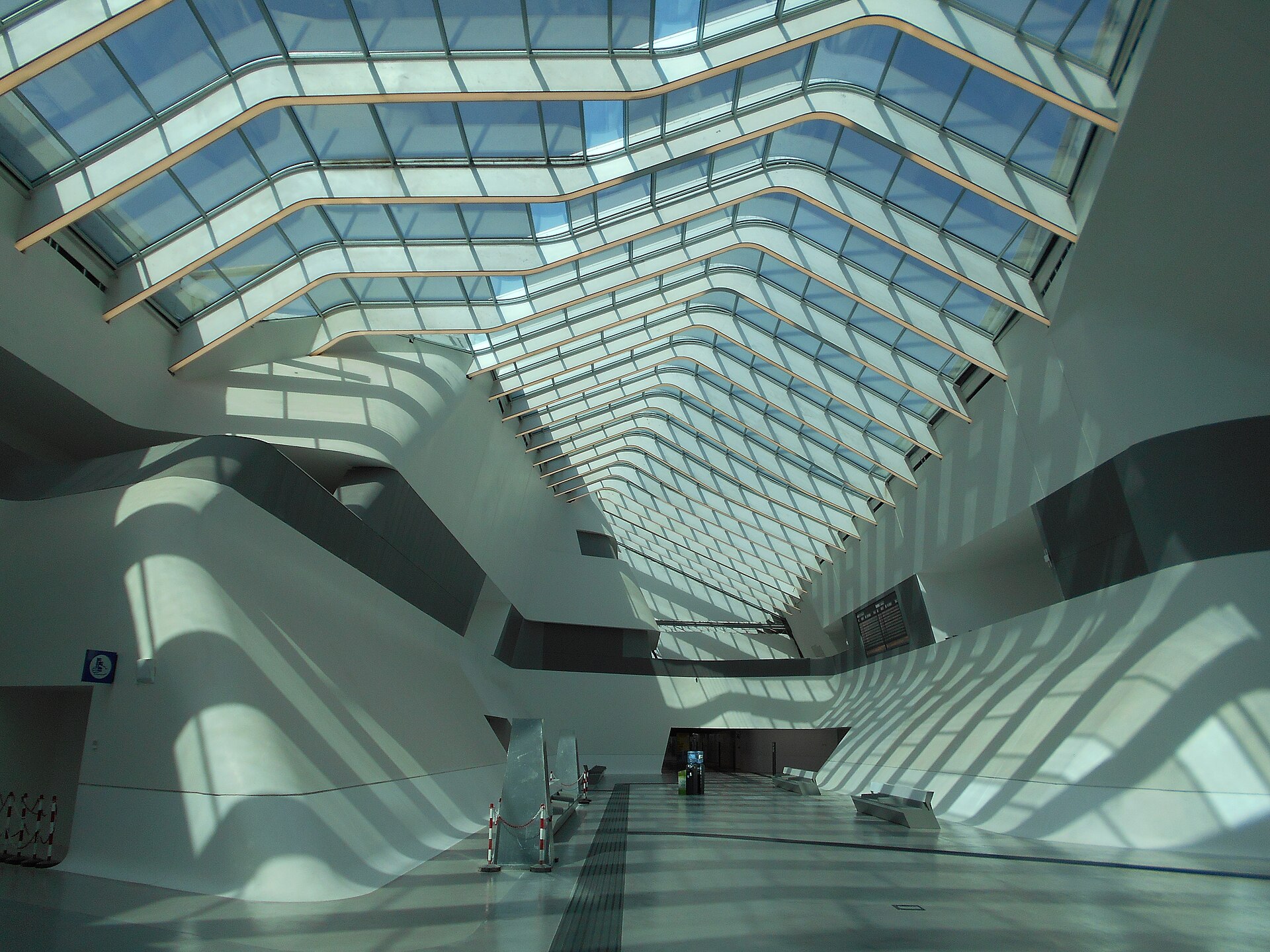 The curving white interior of Napoli Afragola station, with a long glazed roof casting stripes of light across the concourse