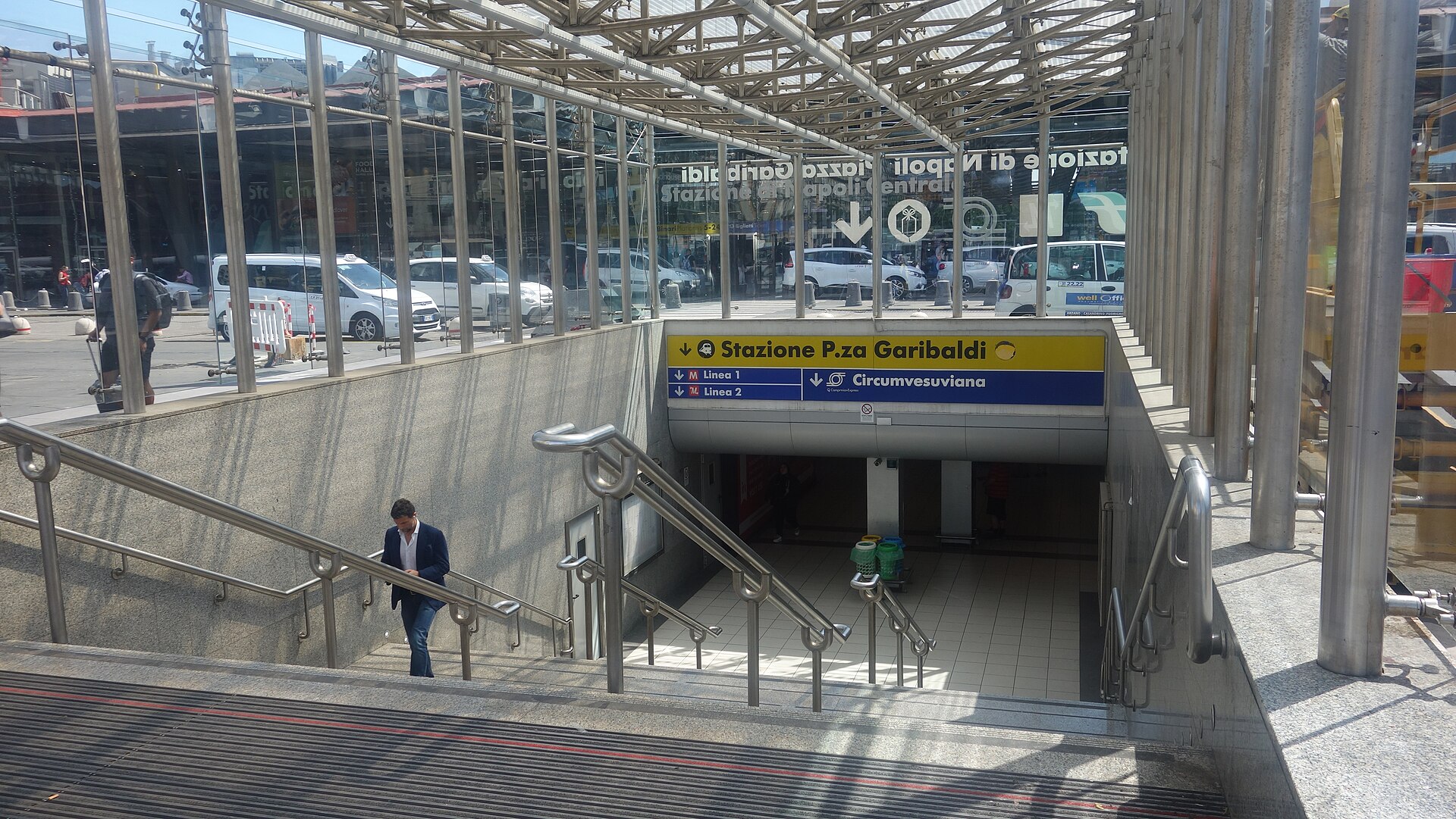 Stairs leading down from Napoli Centrale to the underground Piazza Garibaldi station, with signs pointing to the platforms and to the Circumvesuviana