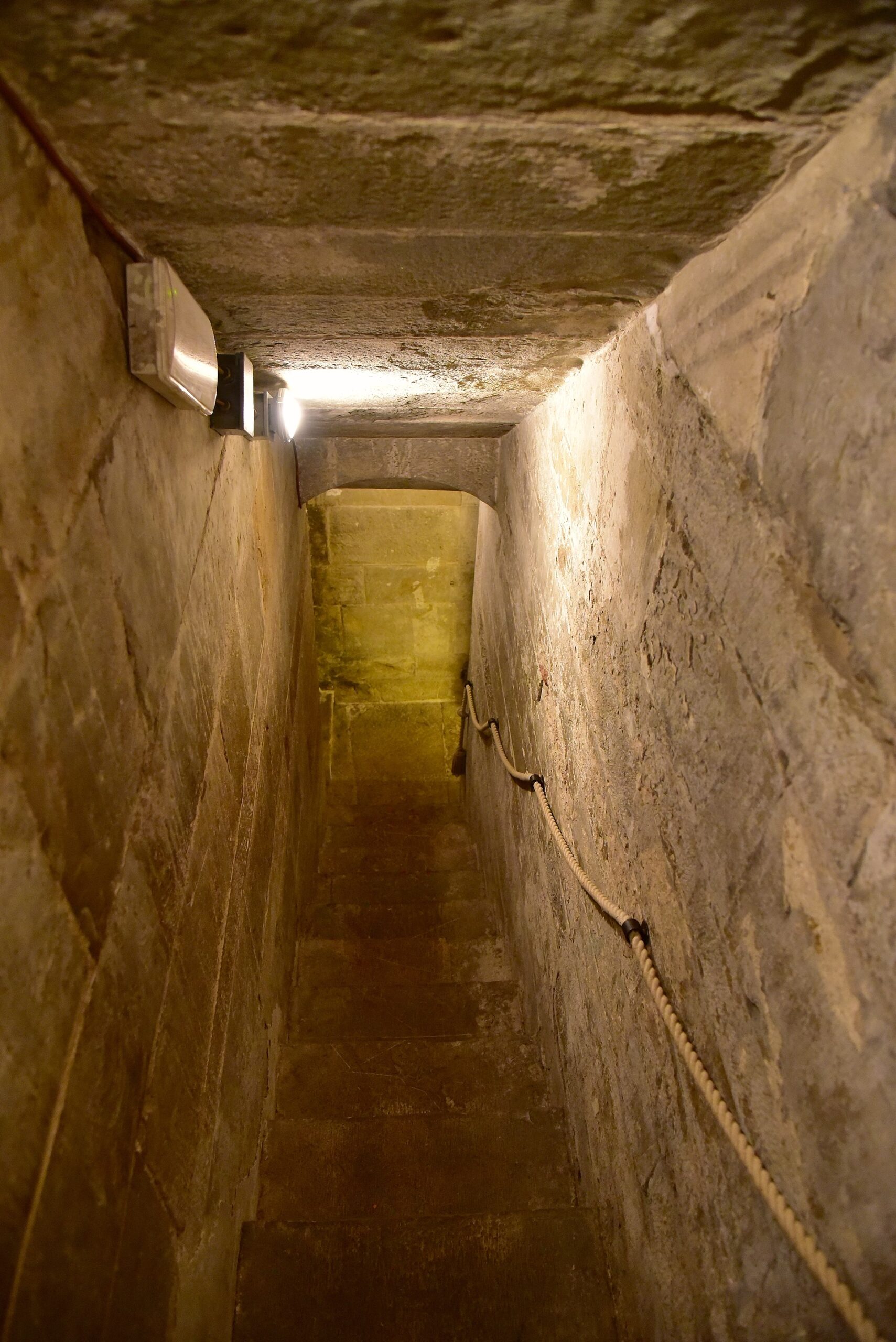A narrow stone staircase descends between rough walls beneath a low ceiling inside Palazzo Vecchio in Florence.