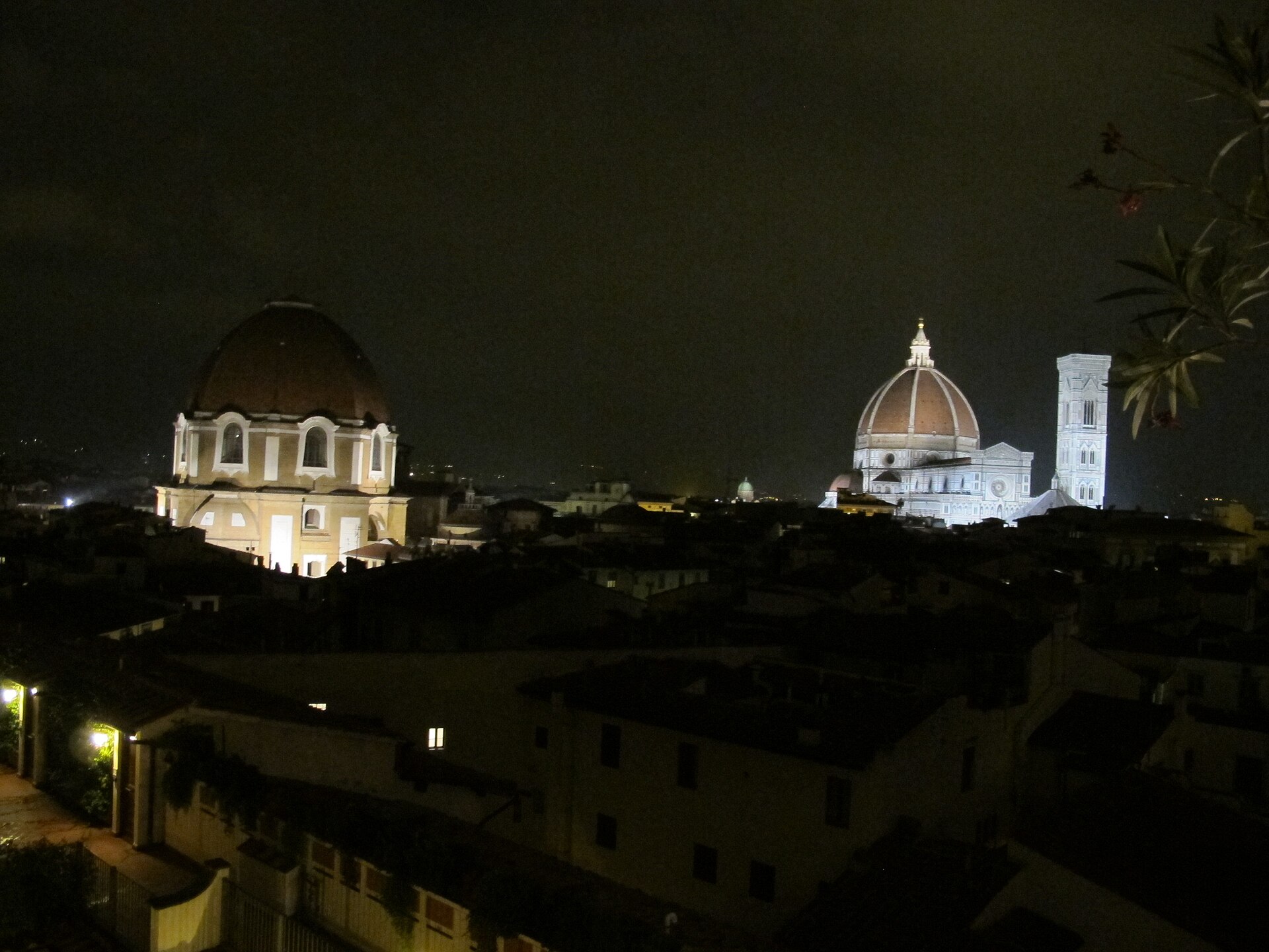 Night view over Florence rooftops from a hotel terrace, with the floodlit Duomo and bell tower and the San Lorenzo dome on the skyline