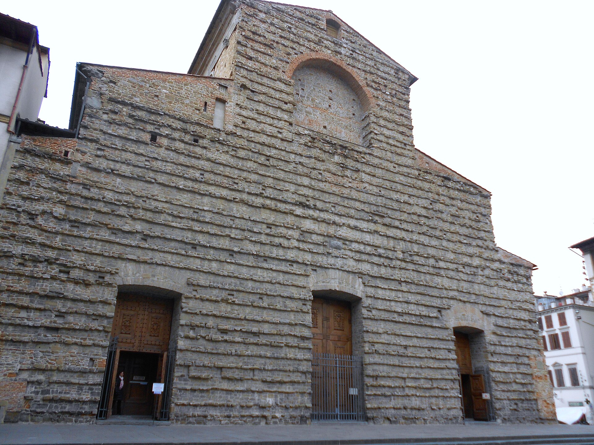 An oblique view shows rough masonry, three doorways and the unfinished upper arch of San Lorenzo basilica in Florence.