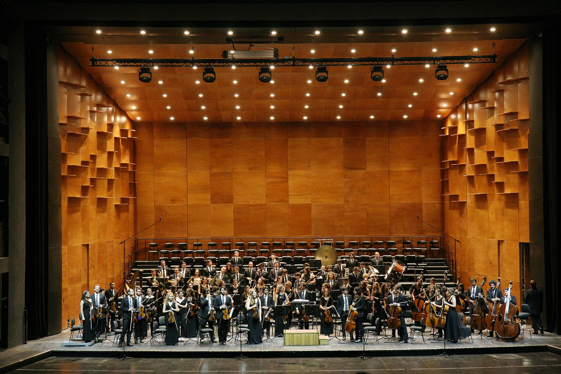 An orchestra gathers on the wood-lined stage of Florence's Teatro del Maggio Musicale Fiorentino beneath warm overhead lights.