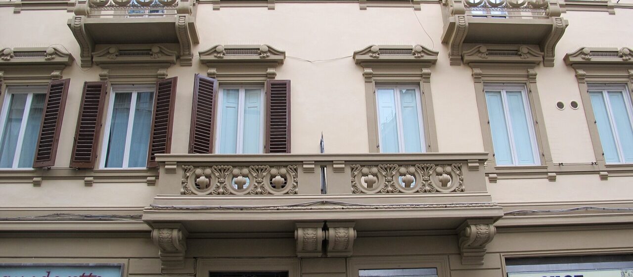 Ornamental balconies and shuttered windows rise above street-level shops on a residential building in Florence’s Via Ghibellina.