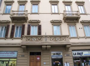 Ornamental balconies and shuttered windows rise above street-level shops on a residential building in Florence’s Via Ghibellina.