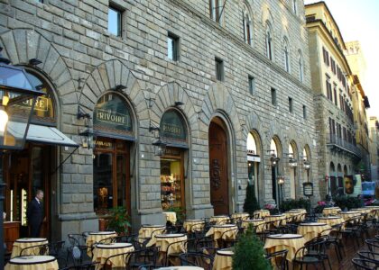 Outdoor tables with yellow cloths in front of the arched, stone-fronted Rivoire café in Florence, its name on the arched signs.