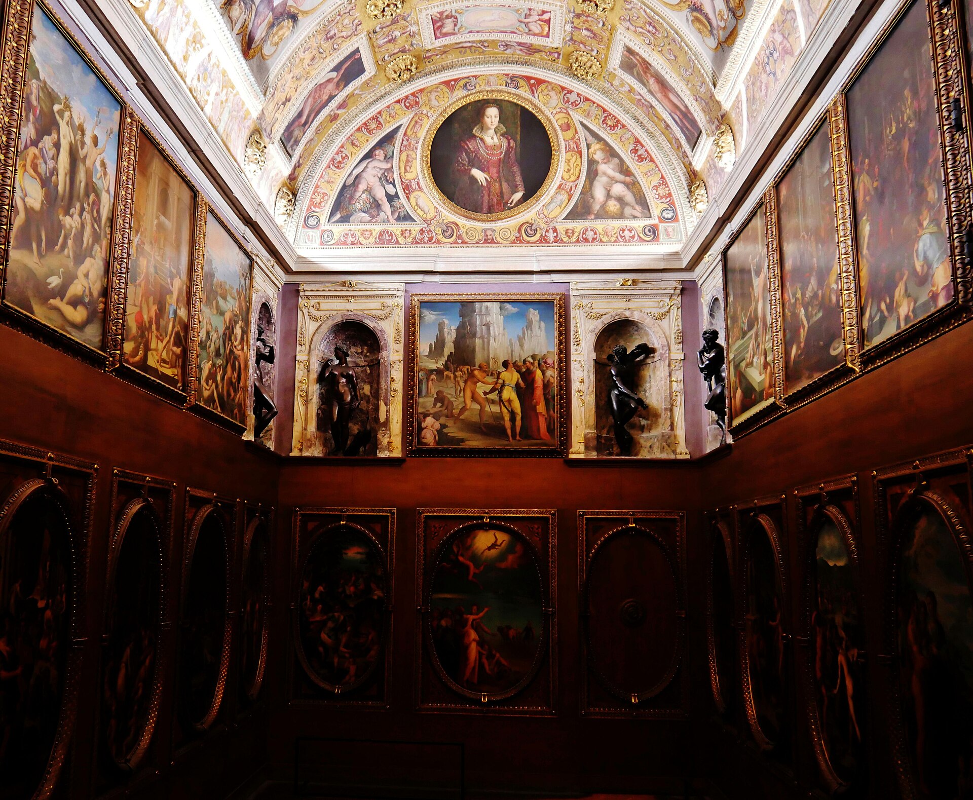 Paintings cover the walls and vaulted ceiling of Francesco I's narrow Studiolo in Florence's Palazzo Vecchio, with bronze statues in niches.