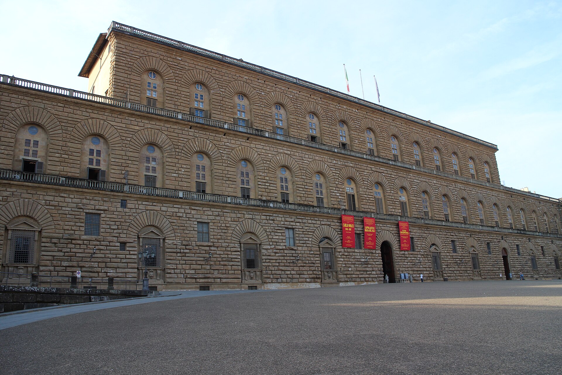 Palazzo Pitti's broad rusticated stone facade rises above the paved Piazza Pitti in Florence, with arched windows and a central doorway.