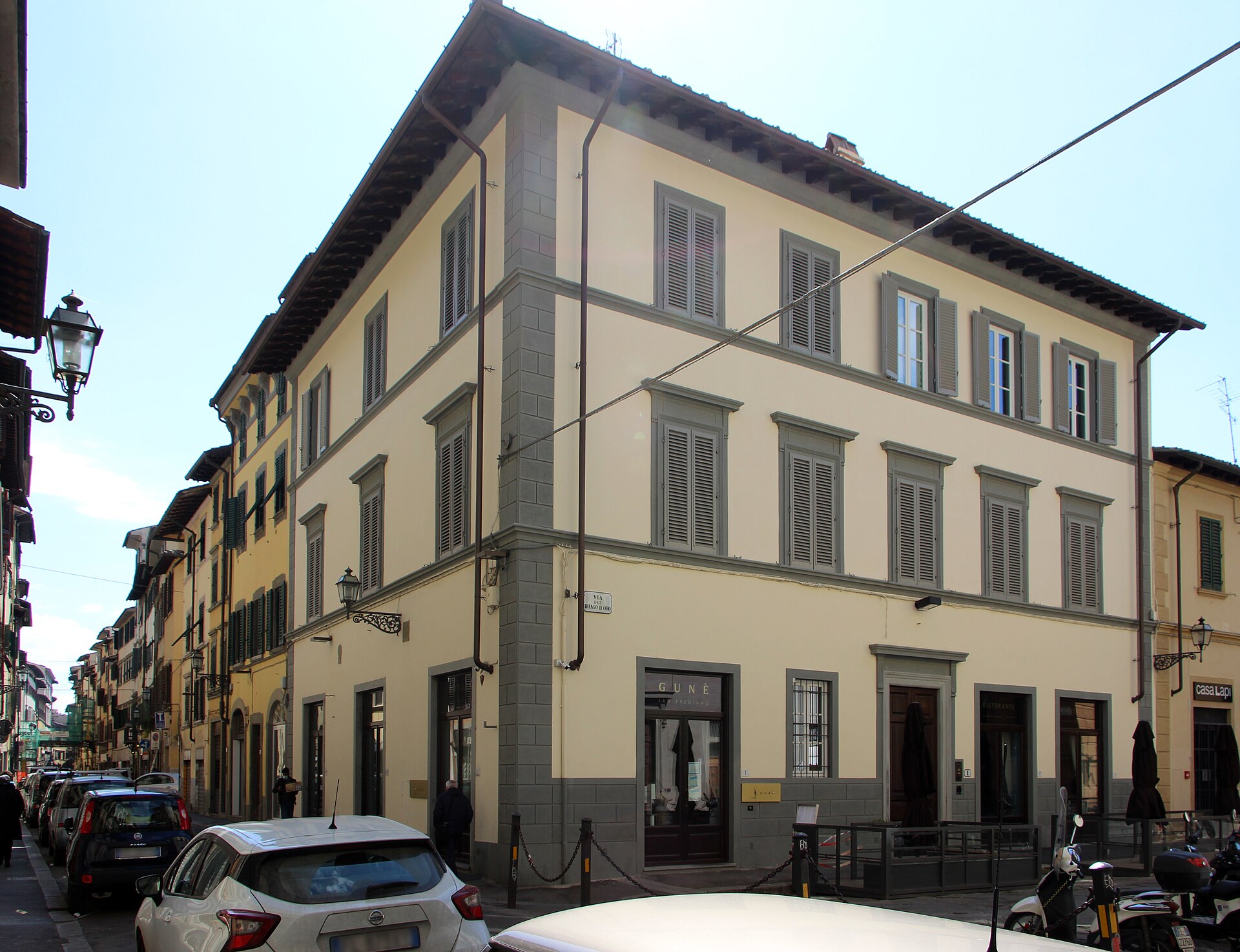 A pale corner building with gray shutters overlooks Borgo San Frediano in Florence’s Oltrarno, beside parked cars.