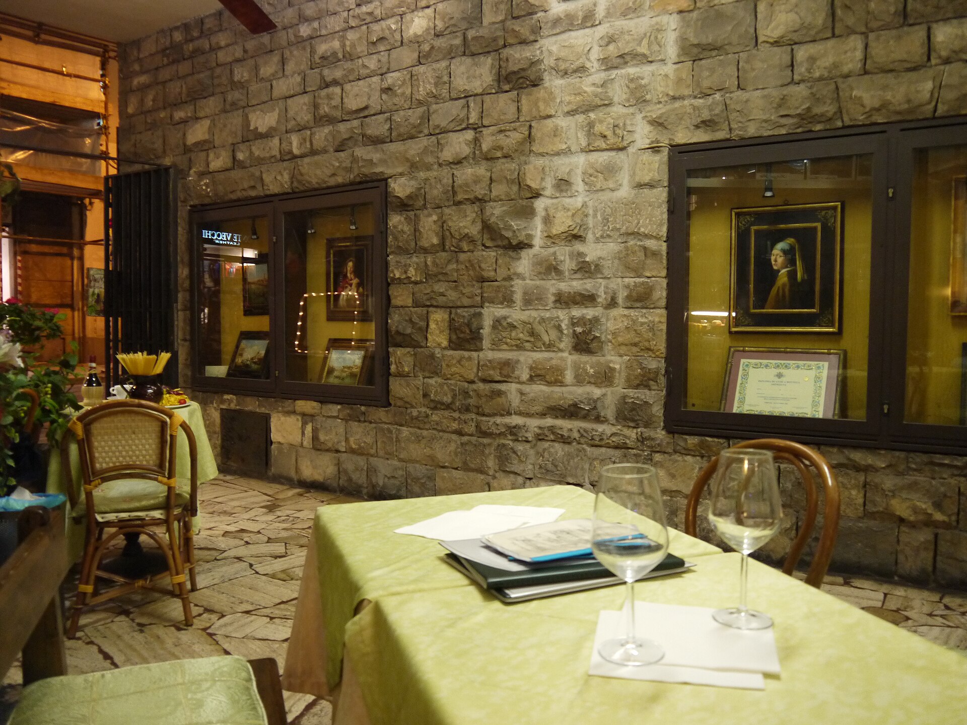 A pale-green restaurant table set with wine glasses and cutlery stands beside a stone wall in Florence.