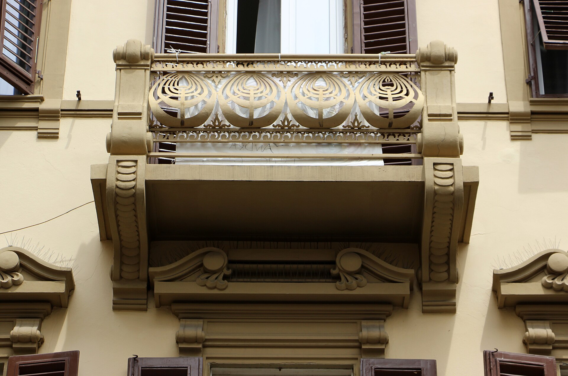 A patterned balcony railing projects between sculpted supports beneath shuttered windows on Florence’s Via Ghibellina.