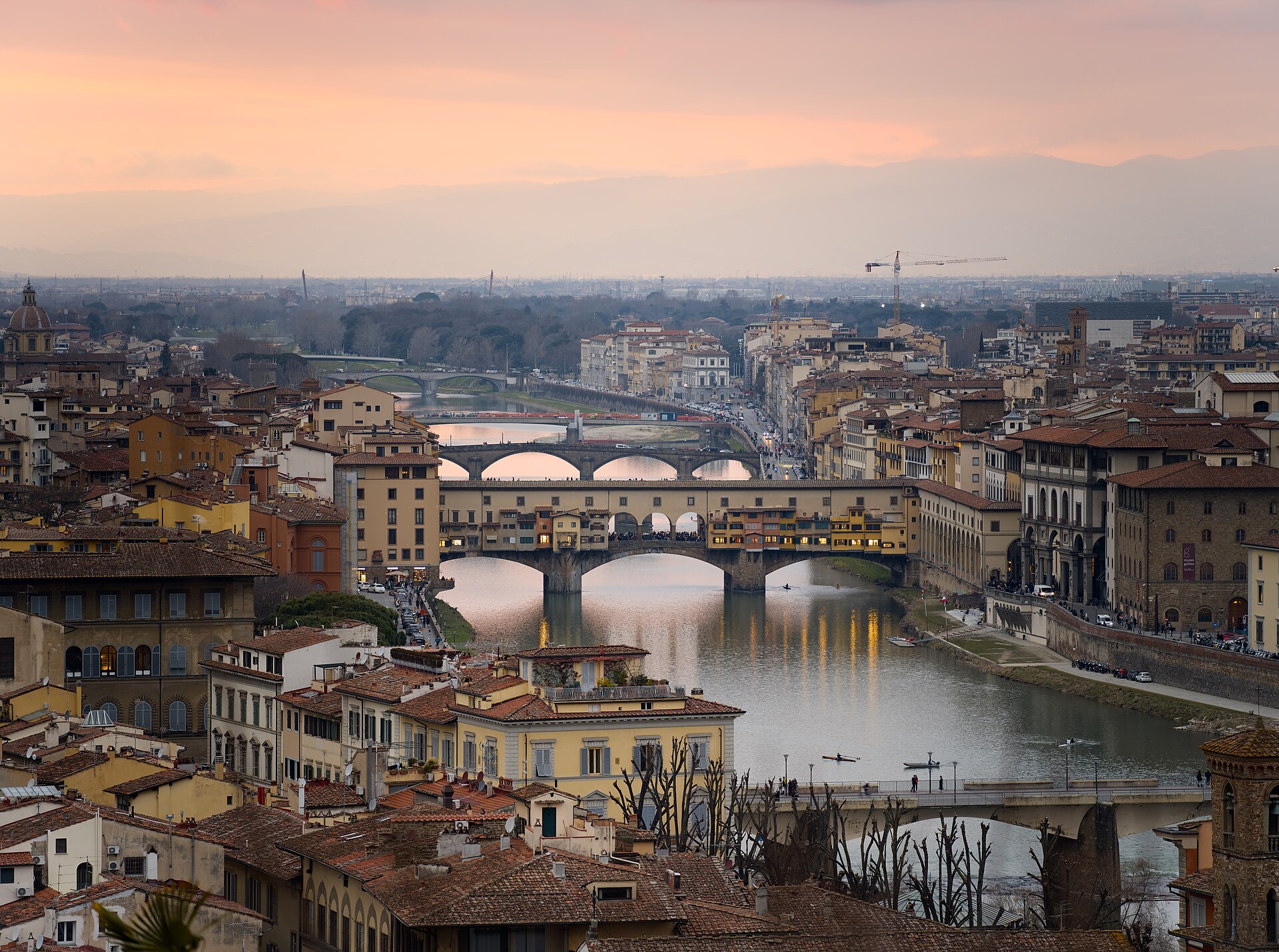 Pink February sunset light reflects along the Arno beneath Ponte Vecchio, seen above Florence’s rooftops from Piazzale Michelangelo.