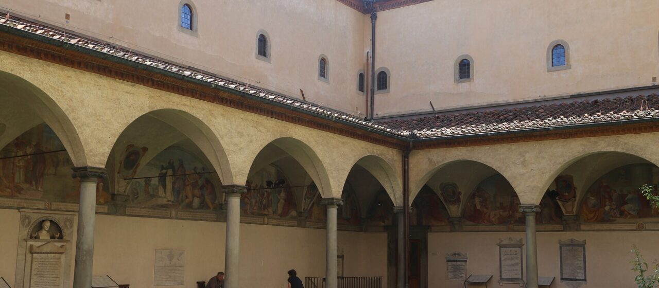 Pink flowers border the arcades and frescoed walls of Sant'Antonino's cloister at the San Marco museum in Florence.