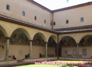 Pink flowers border the arcades and frescoed walls of Sant'Antonino's cloister at the San Marco museum in Florence.