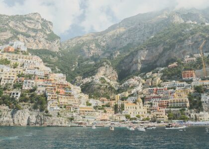 Positano seen from the sea, its pastel houses stacked up a steep green hillside above a small bay with boats moored in the water
