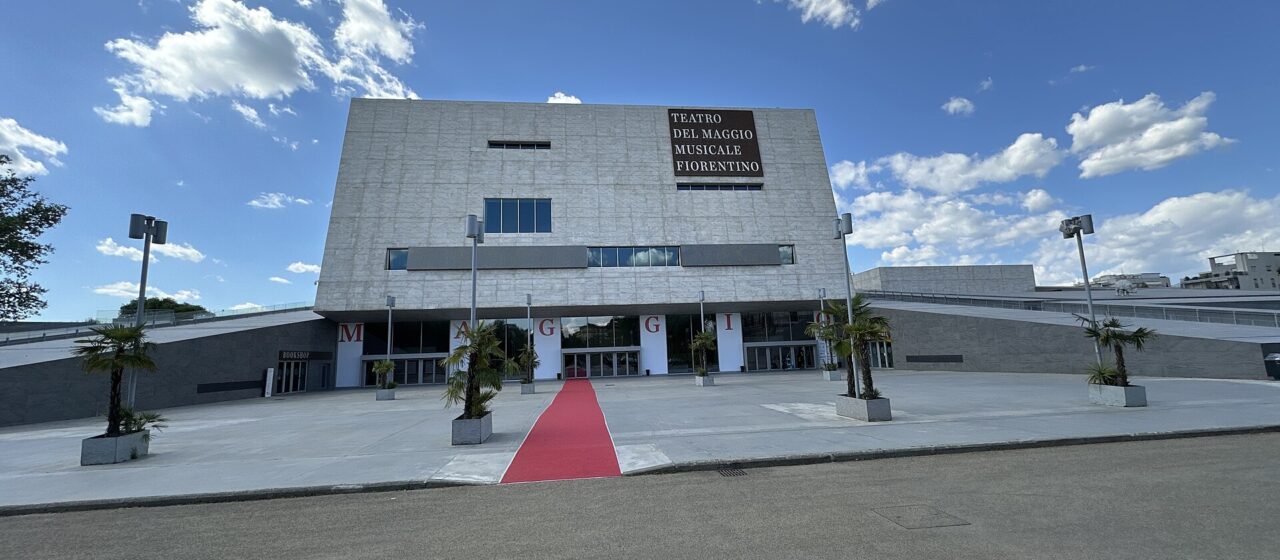 A red carpet leads across the forecourt to Florence's modern Teatro del Maggio Musicale Fiorentino beneath a blue sky.
