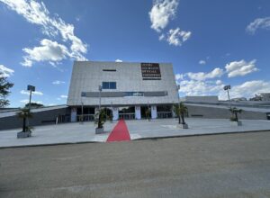 A red carpet leads across the forecourt to Florence's modern Teatro del Maggio Musicale Fiorentino beneath a blue sky.