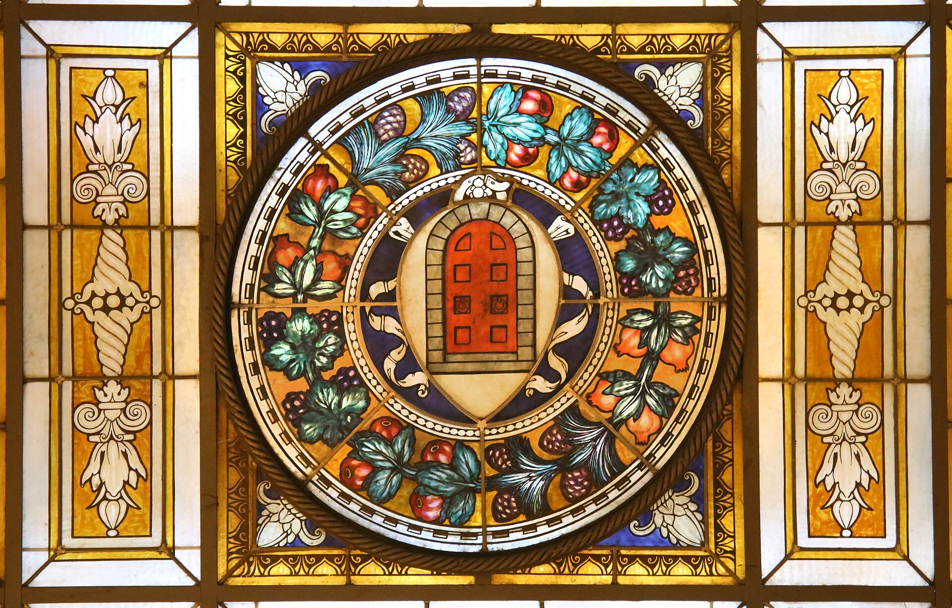 A red door surrounded by colorful leaves and fruit fills a stained-glass panel inside Florence’s Hotel Porta Rossa.