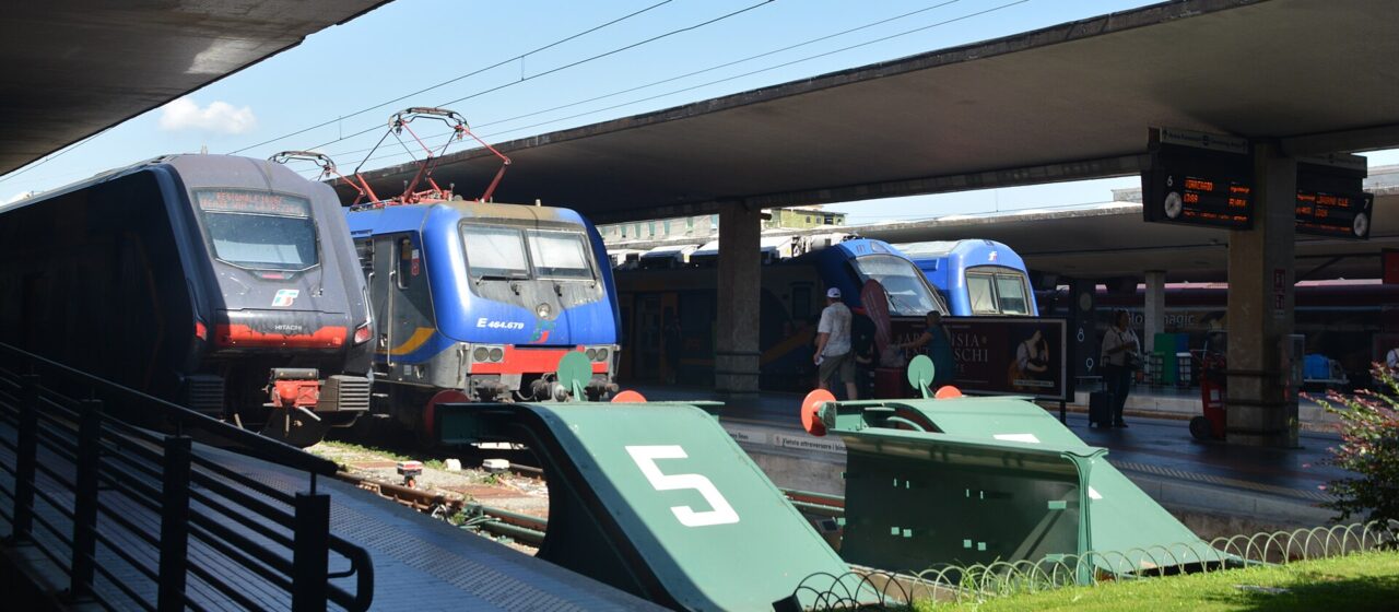 Regional trains stand at the buffer stops of Florence Santa Maria Novella, under concrete canopies and overhead wires.