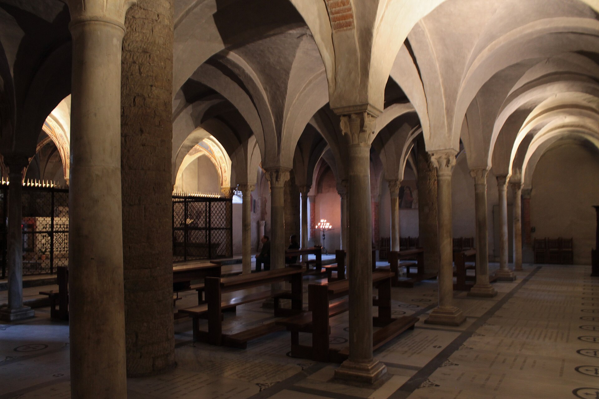 Rows of stone columns support low vaults above wooden benches in the crypt of San Miniato al Monte in Florence.