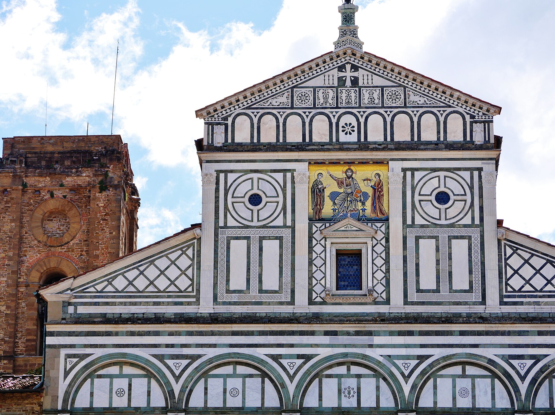 San Miniato al Monte in Florence displays green and white marble panels and a golden mosaic beside its brick bell tower.