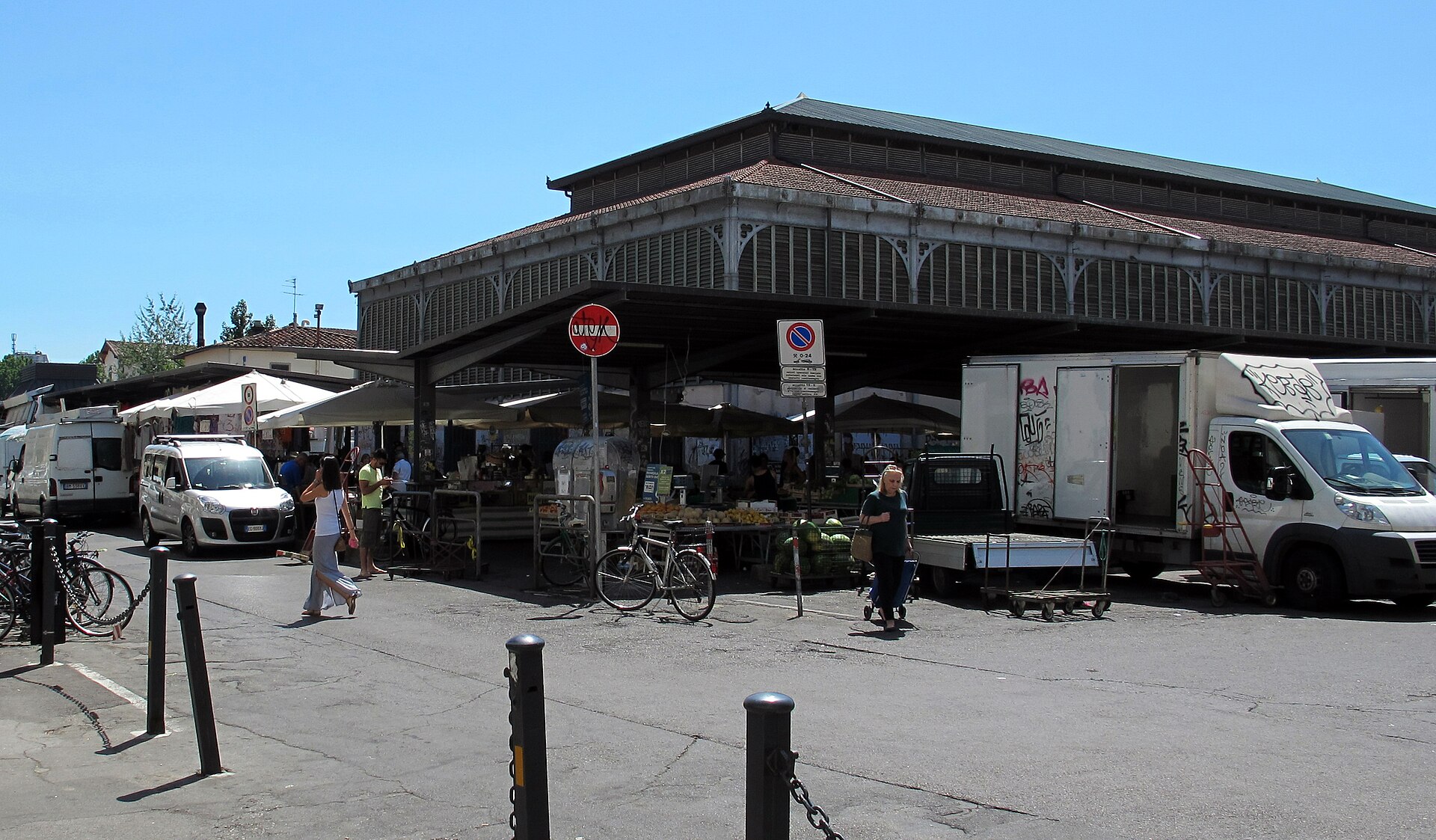 Sant'Ambrogio's market hall shelters outdoor stalls beneath its broad roof, with bicycles, vans and pedestrians in Florence's Piazza Ghiberti.
