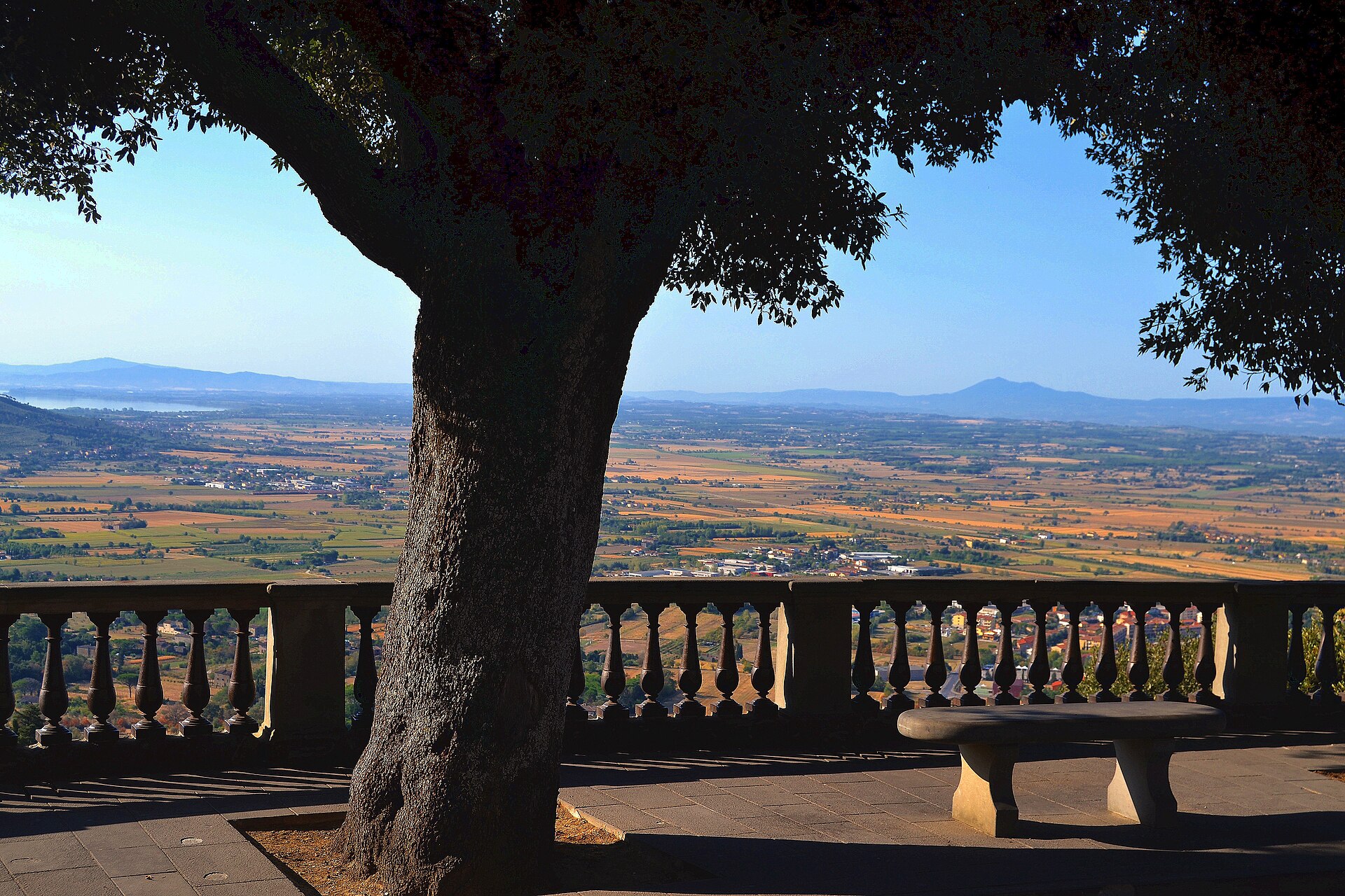 A shaded terrace in Cortona overlooks the Val di Chiana’s fields, with Lake Trasimeno visible in the distance.
