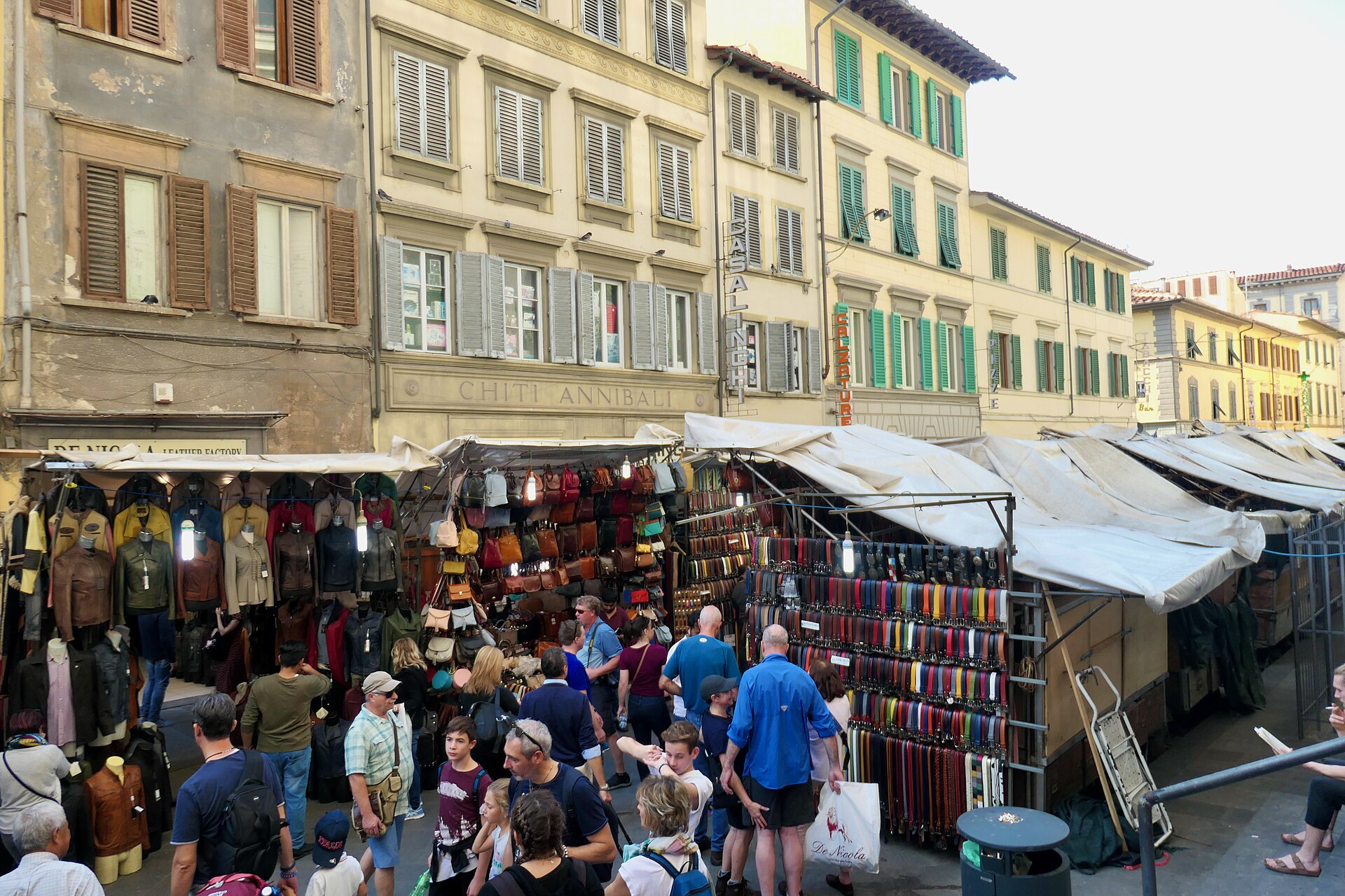 Shoppers browse jackets, handbags and colorful belts at outdoor stalls in Florence's San Lorenzo market.