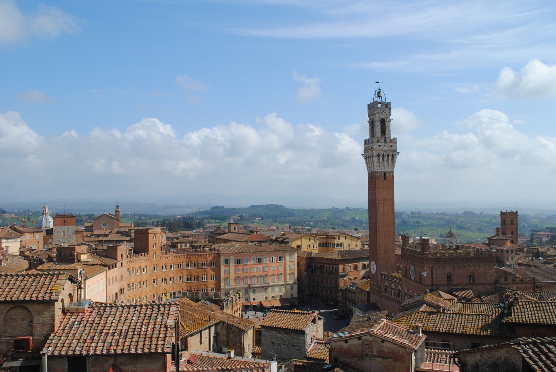 View over Siena's terracotta rooftops to the Torre del Mangia, with the Tuscan countryside stretching to the horizon