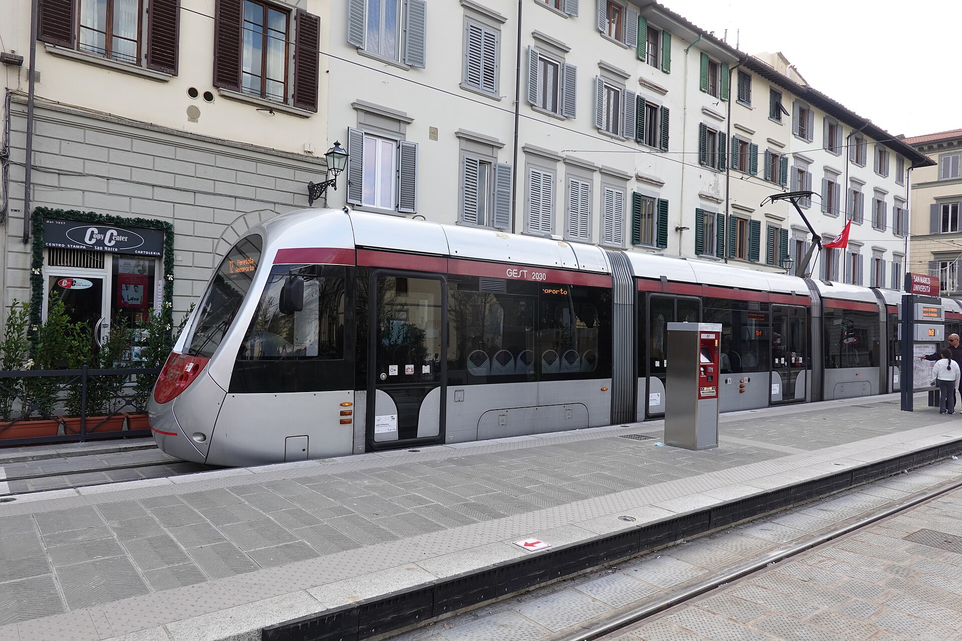 A silver and red Florence tram stands beside a raised platform with tactile paving and a ticket machine.