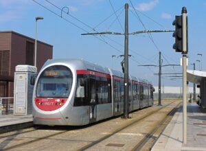 A silver and red T2 tram waits between the platforms at Florence Airport beneath overhead wires and blue sky.