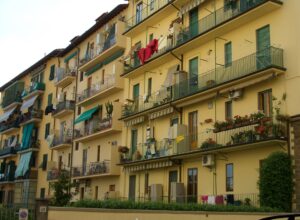 Stacked balconies, green shutters, flower boxes and drying laundry cover a yellow apartment building in Florence.