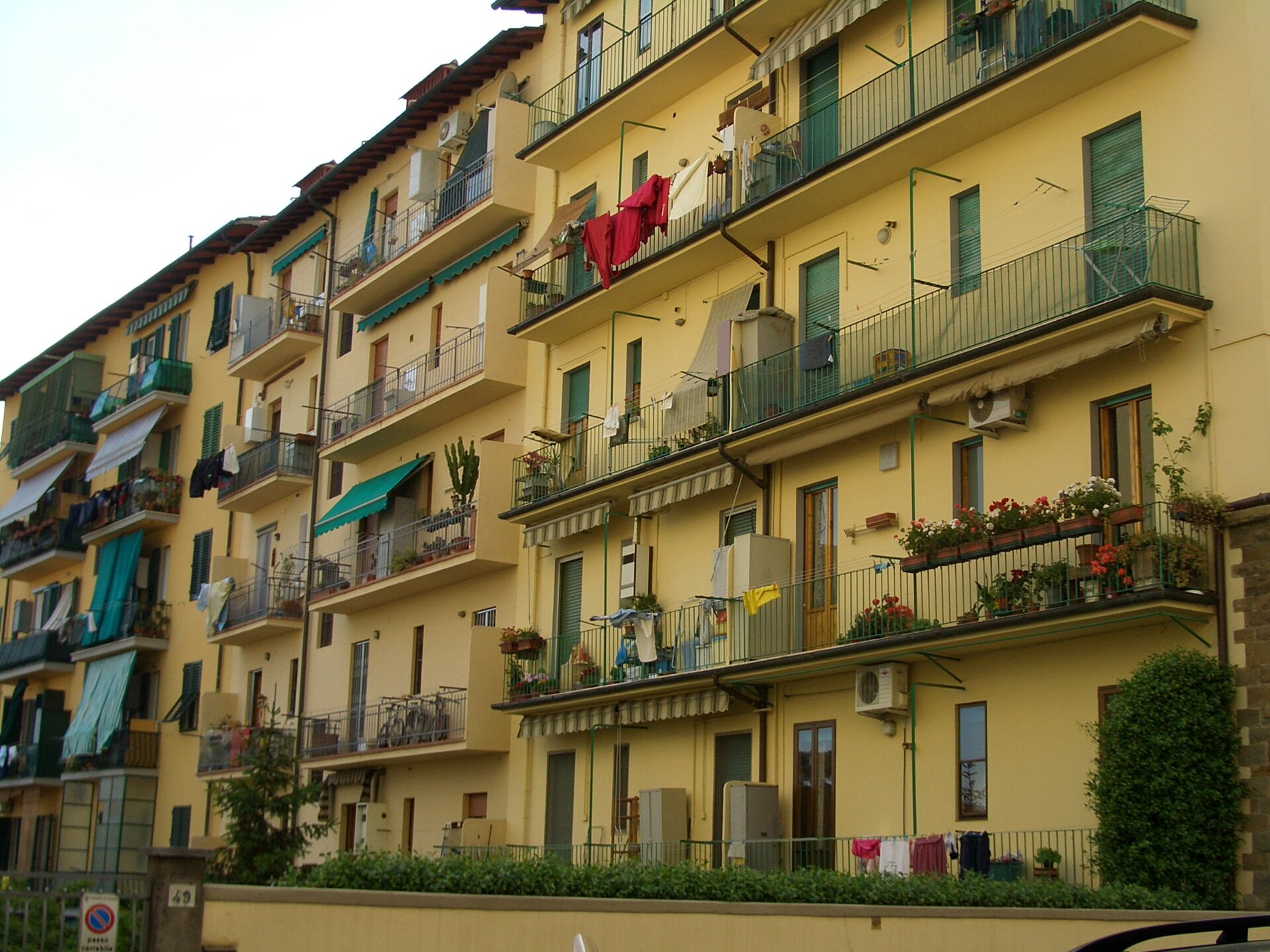 Stacked balconies, green shutters, flower boxes and drying laundry cover a yellow apartment building in Florence.