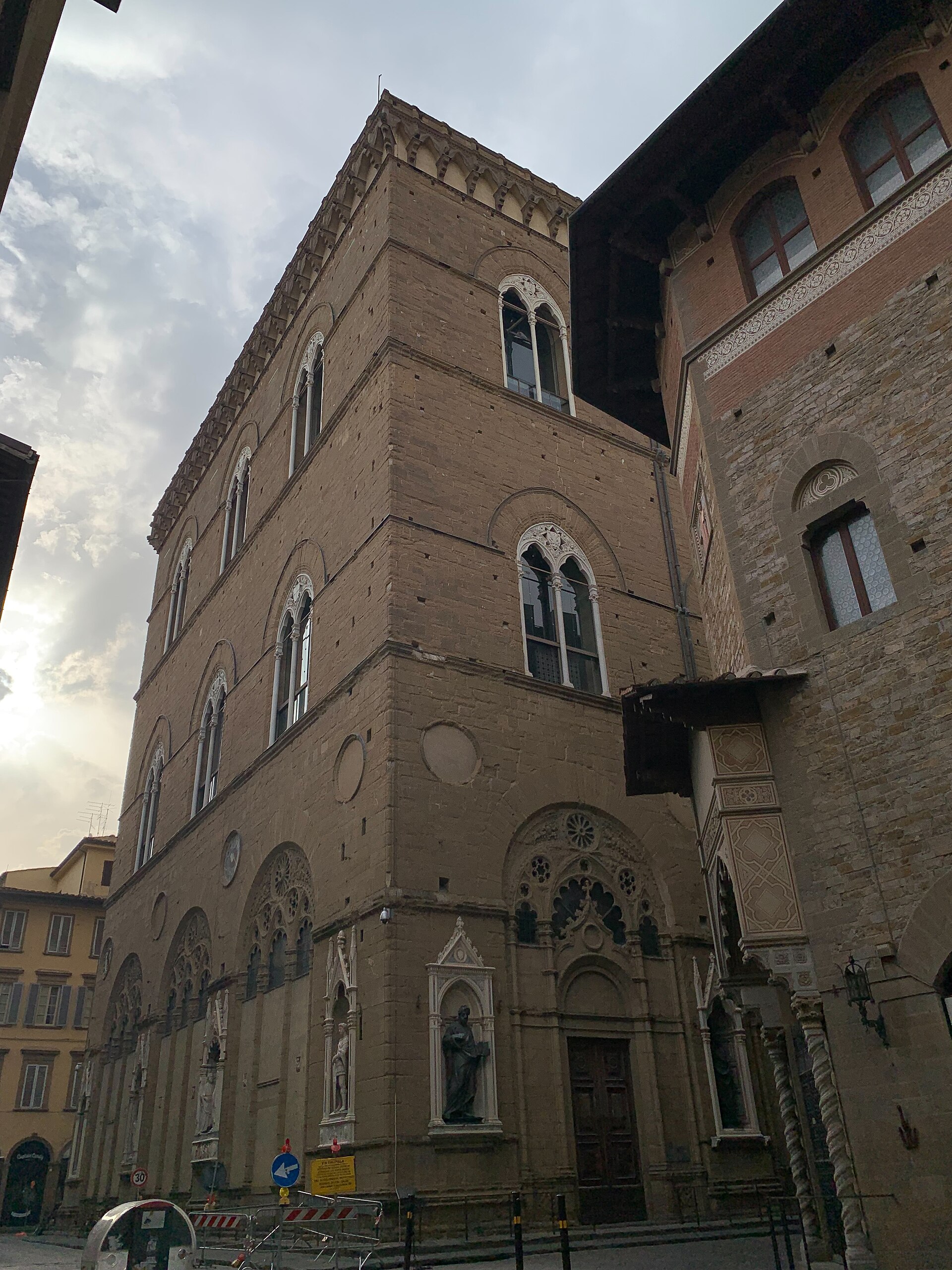 Statues occupy ornate street-level niches beneath the pointed windows of Orsanmichele's stone exterior in Florence.