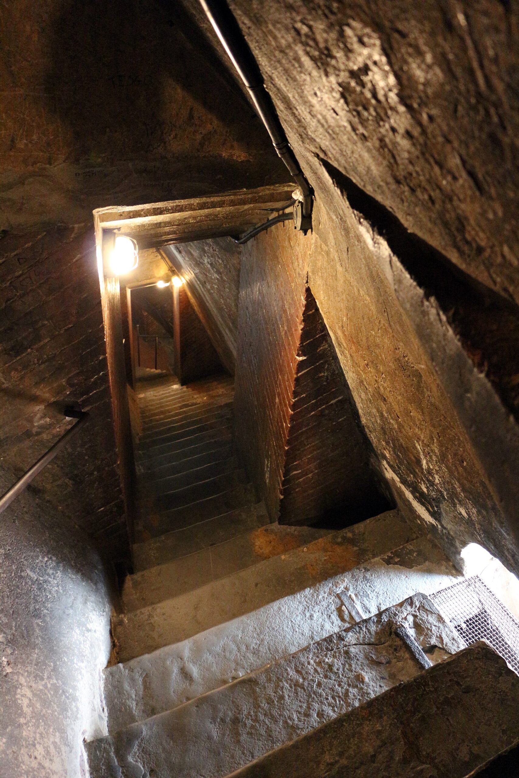 Steep stone steps descend between curving brick walls inside Brunelleschi's dome in Florence, with metal handrails and a low overhead passage.